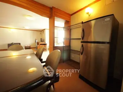 Spacious kitchen with stainless steel fridge and dining area in modern apartment.
