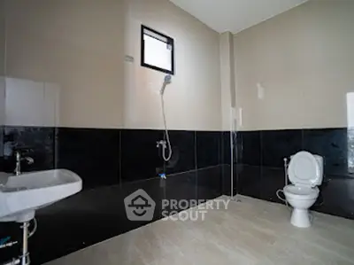 Spacious modern bathroom with sleek black and beige tiles, featuring a shower and toilet.