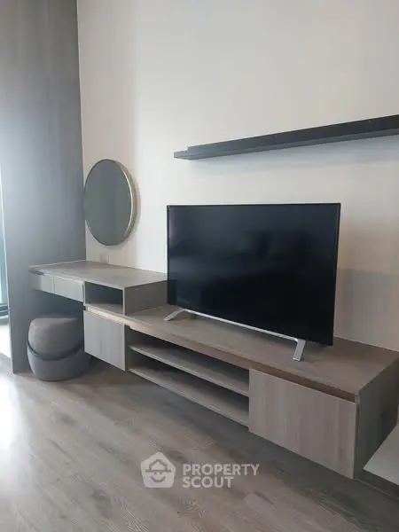 Modern living room with sleek TV stand and round mirror on wooden flooring.