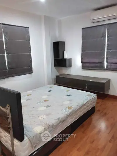 Modern bedroom with wooden flooring and stylish blinds, featuring a sleek bed and air conditioning.