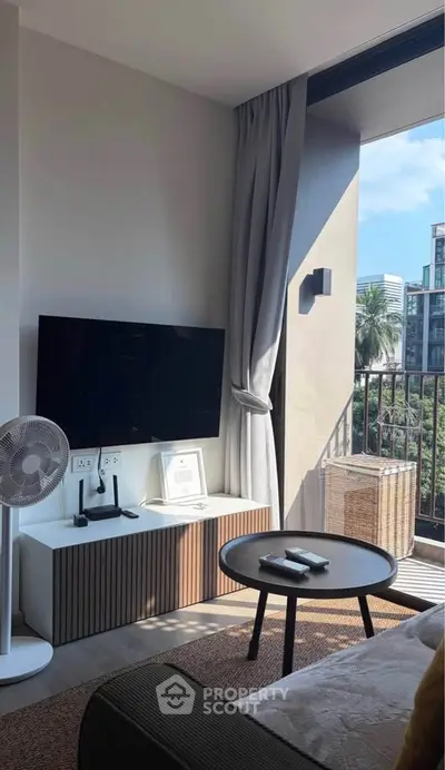 Modern living room with balcony view, featuring sleek TV setup and stylish decor.