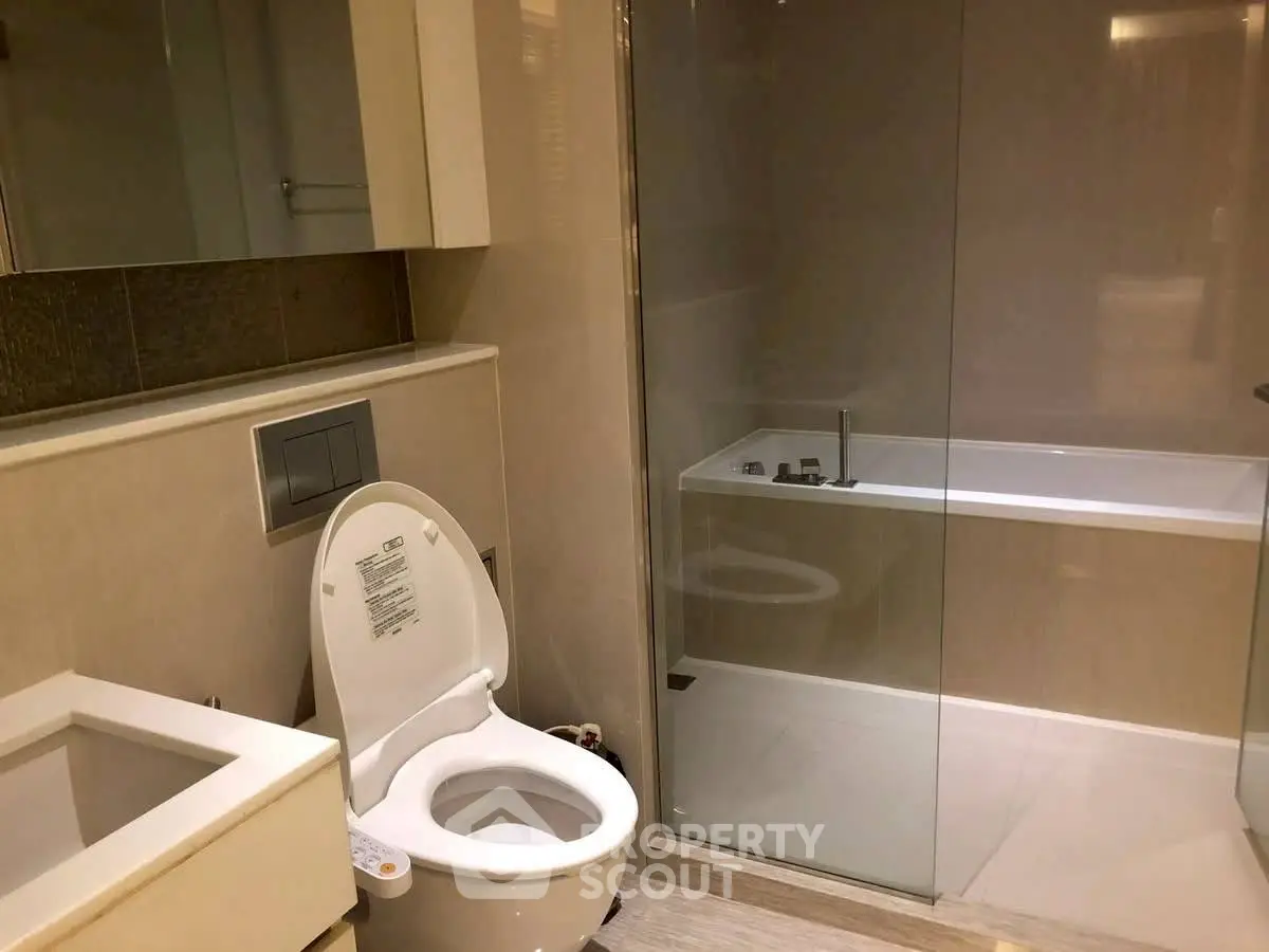 Modern bathroom with sleek design, featuring a glass-enclosed bathtub and contemporary fixtures.