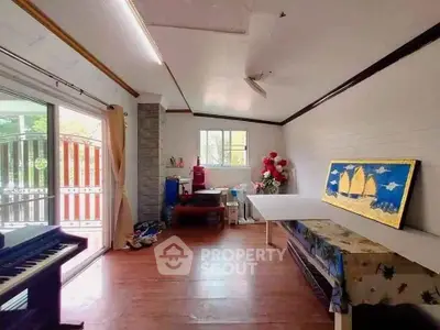 Spacious living room with wooden flooring and large window, featuring a piano and decorative wall art.