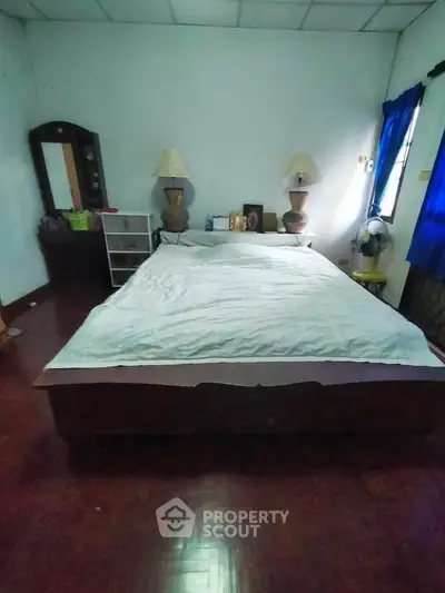 Cozy bedroom with wooden flooring and natural light, featuring a large bed and elegant lamps.