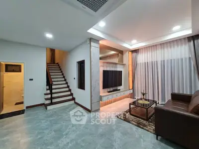 Modern living room with stylish decor and staircase, featuring a large TV and cozy seating area.