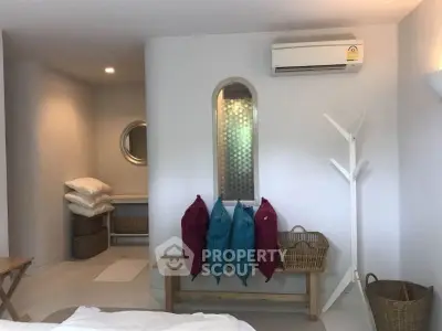 Charming bedroom with modern decor and air conditioning, featuring cozy seating and stylish storage solutions.