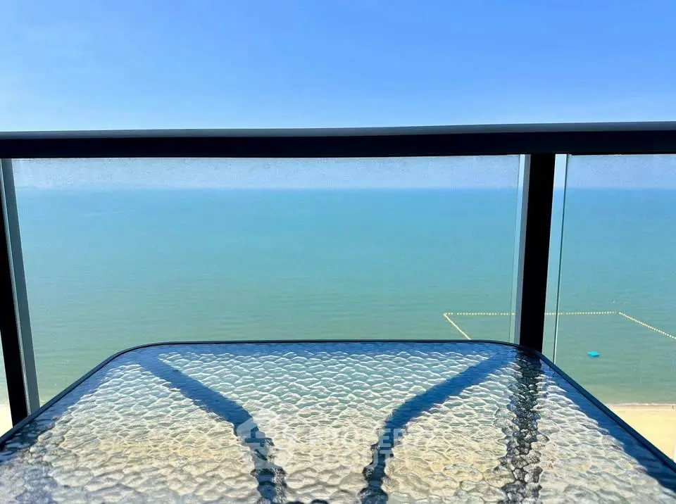 Stunning ocean view from a modern balcony with glass railing and table.