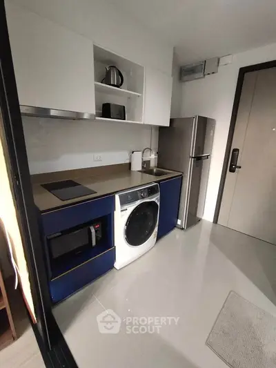 Modern kitchen with sleek appliances and compact design, featuring a washing machine and fridge.