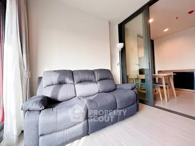 Modern living room with cozy gray sofa and sliding glass doors leading to dining area.