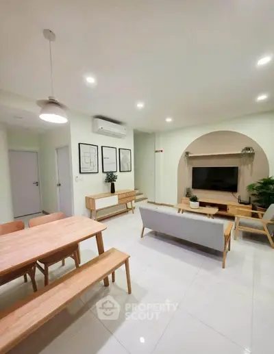Modern living room with minimalist decor and open dining area, featuring sleek furniture and bright lighting.