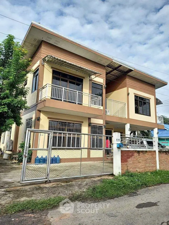 Modern two-story house with spacious balcony and gated entrance in a serene neighborhood.