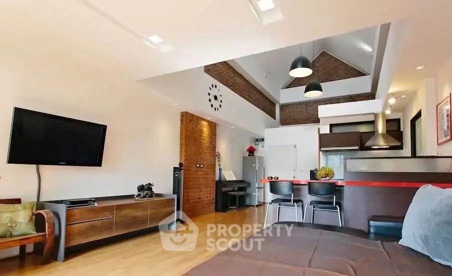 Modern living room with high ceiling and stylish decor, featuring a wall-mounted TV and open kitchen layout.