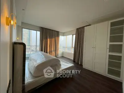 Spacious bedroom with large windows and city view, featuring modern furniture and ample natural light.