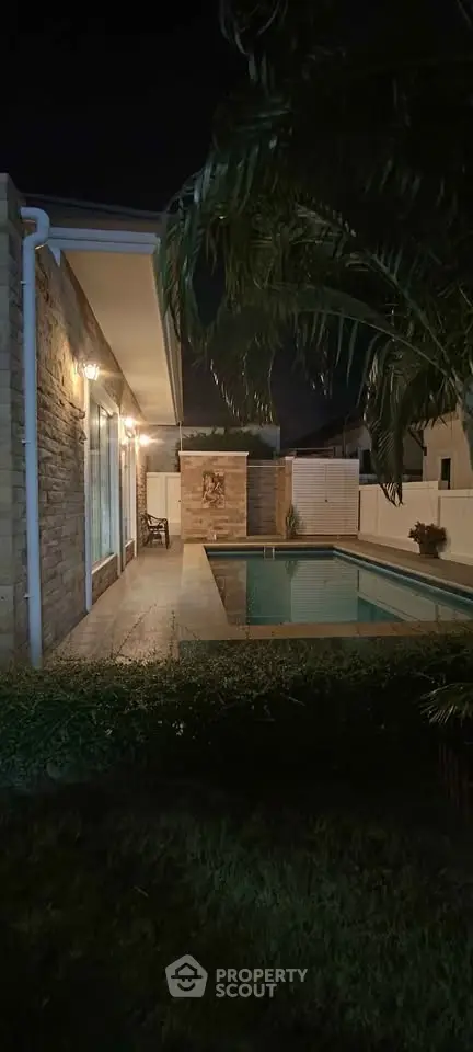 Stunning night view of a modern home with a beautifully lit pool and lush greenery.