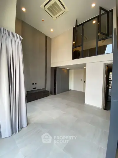 Spacious modern living room with high ceiling and mezzanine, featuring sleek design and ample natural light.