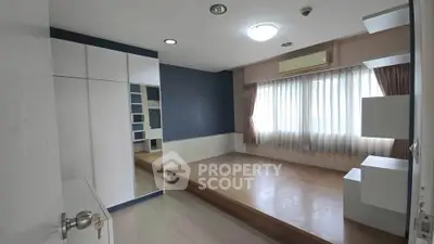 Spacious bedroom with elevated wooden platform and large window for natural light.