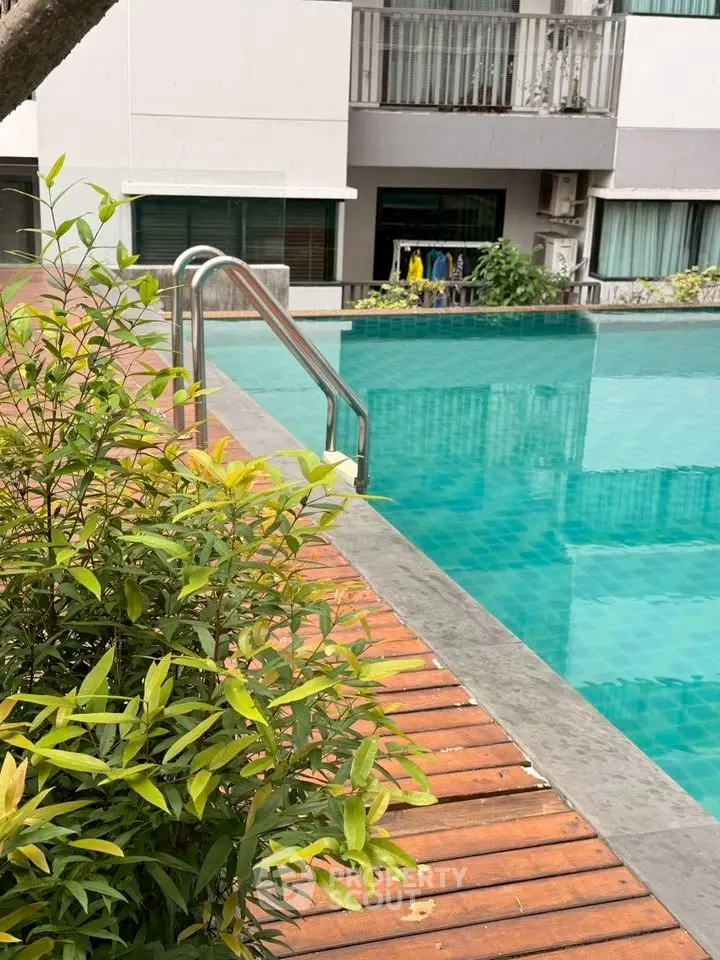 Luxurious poolside view with lush greenery and modern apartment backdrop.
