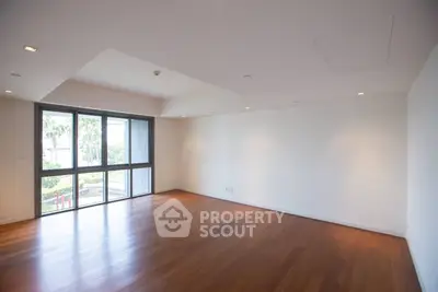 Spacious empty living room with wooden flooring and large windows offering natural light and garden view.