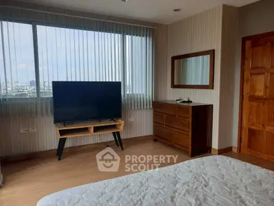 Spacious bedroom with large window and city view, featuring modern TV and wooden furniture.