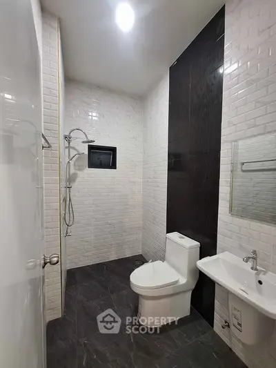 Modern bathroom with sleek design, featuring a shower, toilet, and sink with stylish tiles.