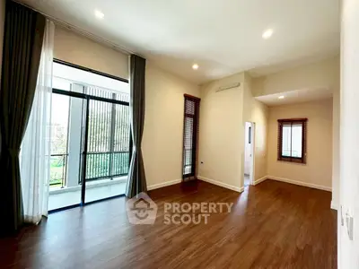 Spacious living room with large windows and balcony access, featuring elegant wooden flooring.