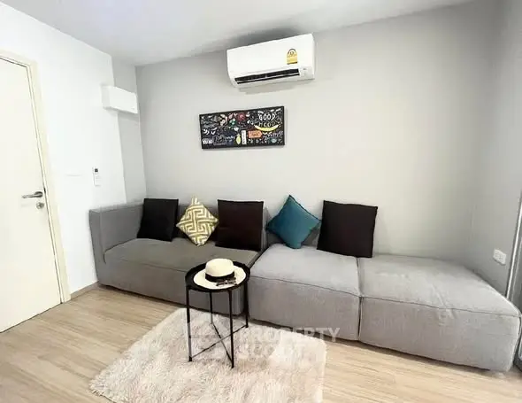Modern living room with stylish gray sofa, wall art, and air conditioning unit.