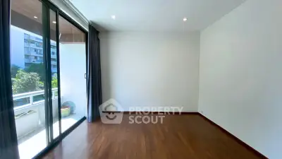 Spacious empty room with wooden flooring and large sliding glass doors leading to a balcony with a view.