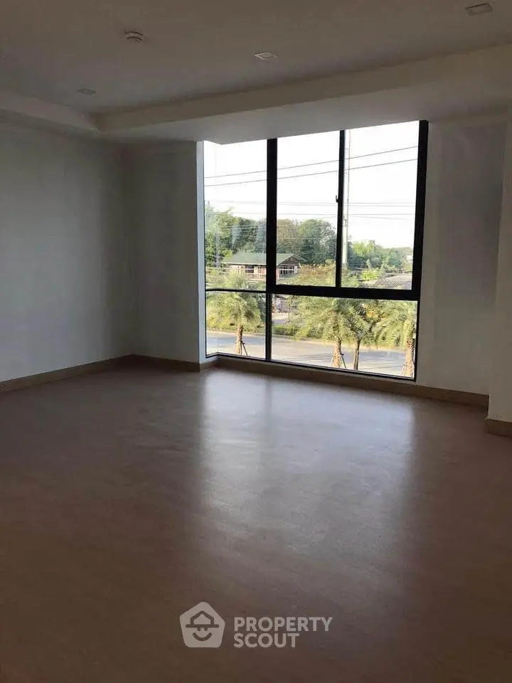 Spacious empty room with large window offering scenic views of greenery and street.