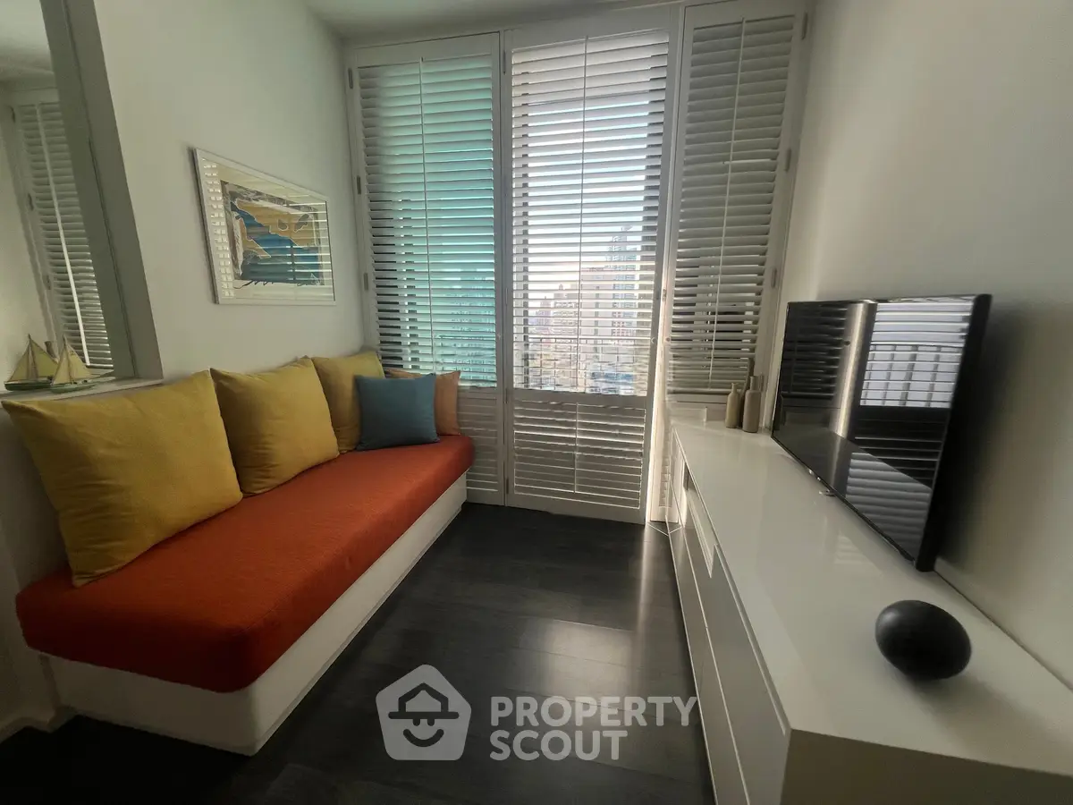 Modern living room with sleek design, featuring a cozy sofa, wall-mounted TV, and large windows with blinds.