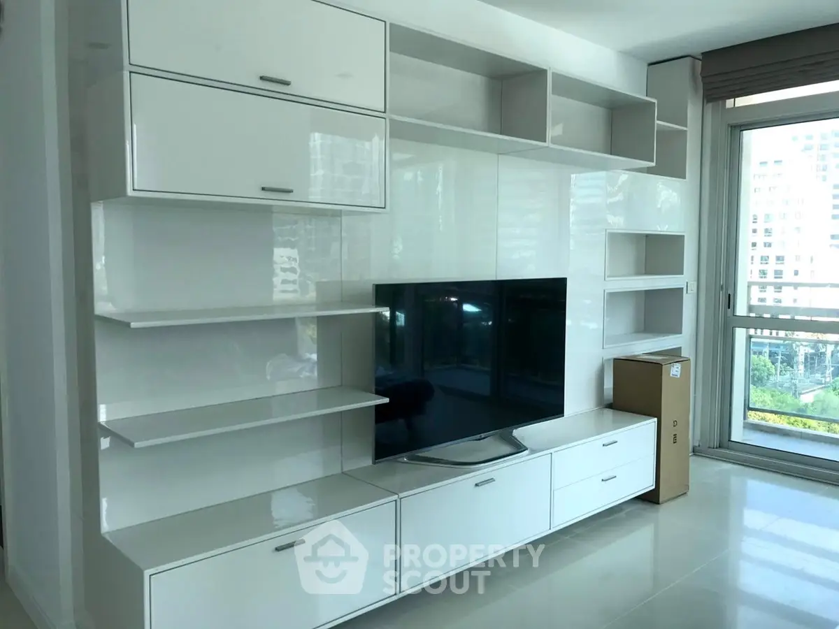 Modern living room with sleek white entertainment unit and large windows offering city views.