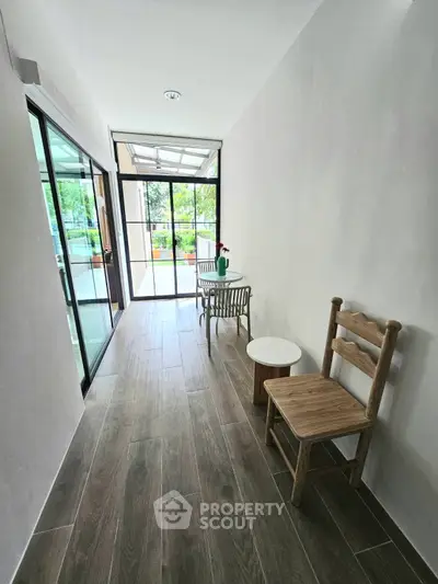 Charming hallway with wooden flooring and glass doors leading to a lush garden view.