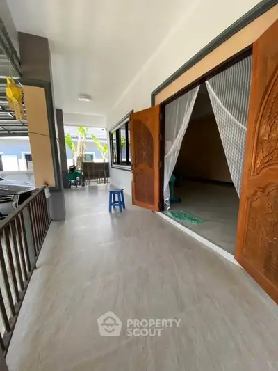 Spacious covered balcony with elegant wooden doors and tiled flooring, perfect for relaxation.