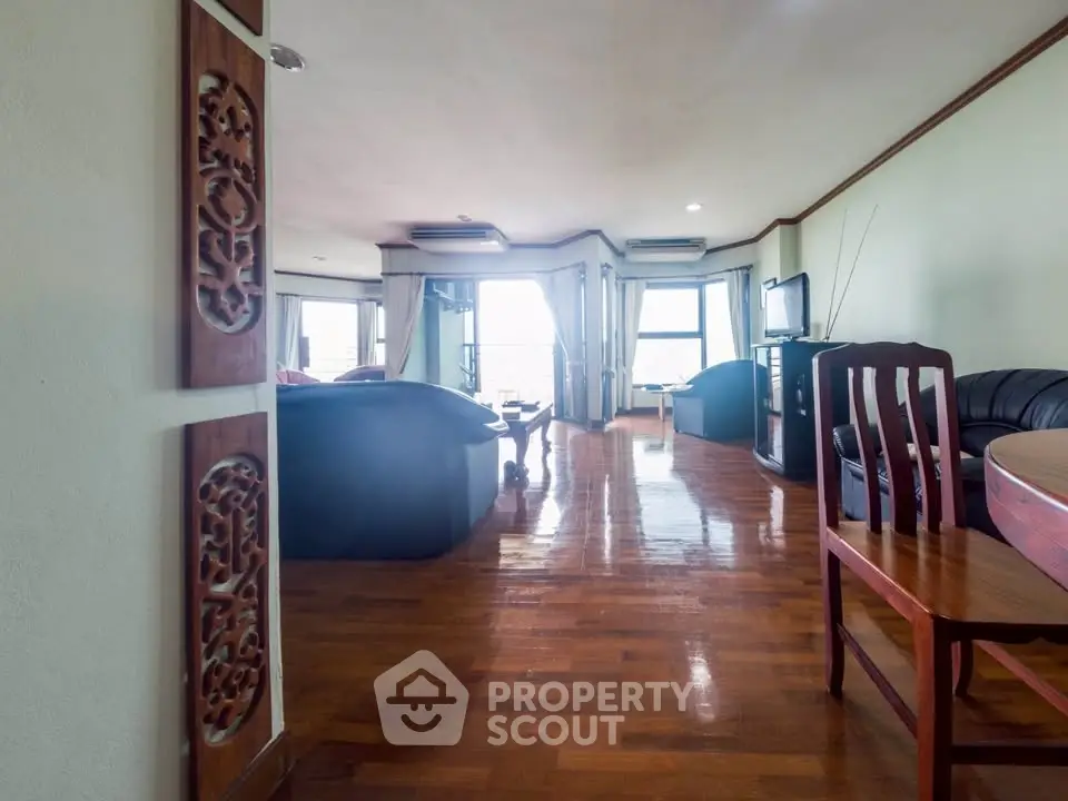 Spacious living room with wooden flooring and elegant decor, featuring a cozy seating area and large windows.