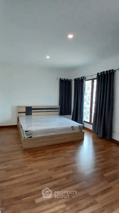 Spacious bedroom with wooden flooring and large windows for natural light.