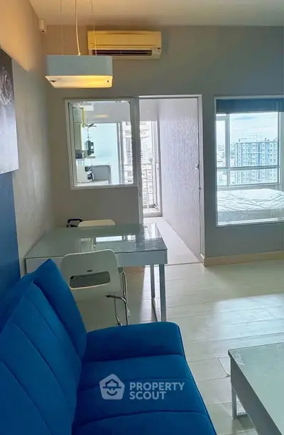 Modern apartment interior with blue sofa, glass table, and city view from the window.