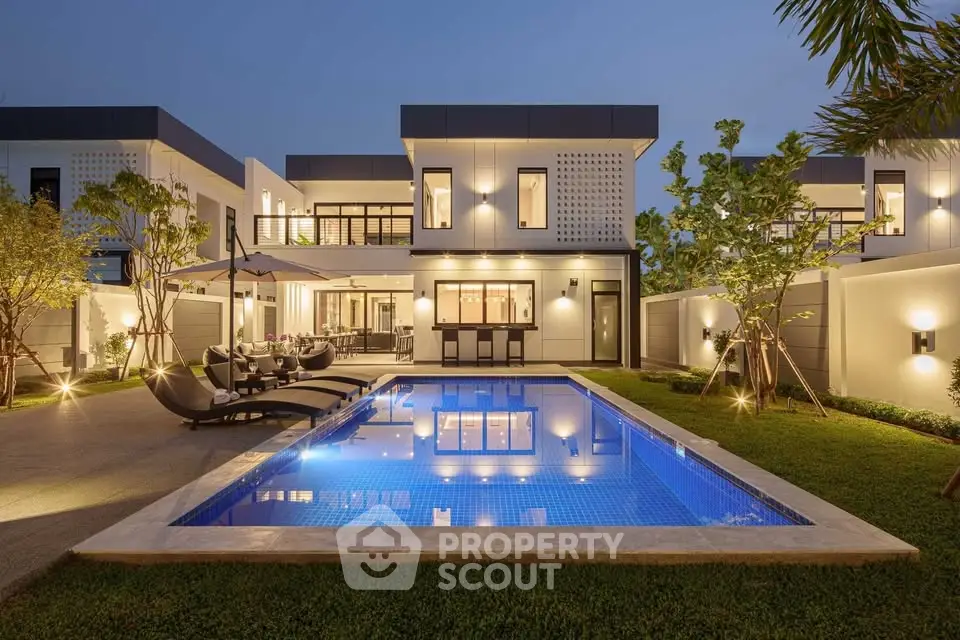 Luxurious modern villa with illuminated pool and elegant outdoor dining area at dusk.