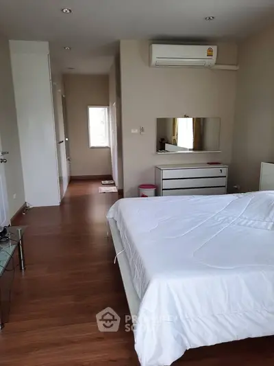 Spacious bedroom with modern decor and wooden flooring, featuring a large bed and air conditioning.