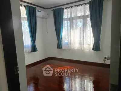 Bright empty room with polished wooden floors and large windows with blue curtains.