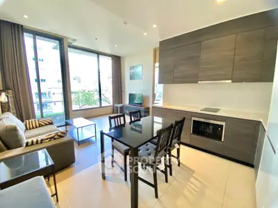 Modern open-layout living room with kitchen, featuring sleek cabinetry and large windows for natural light.