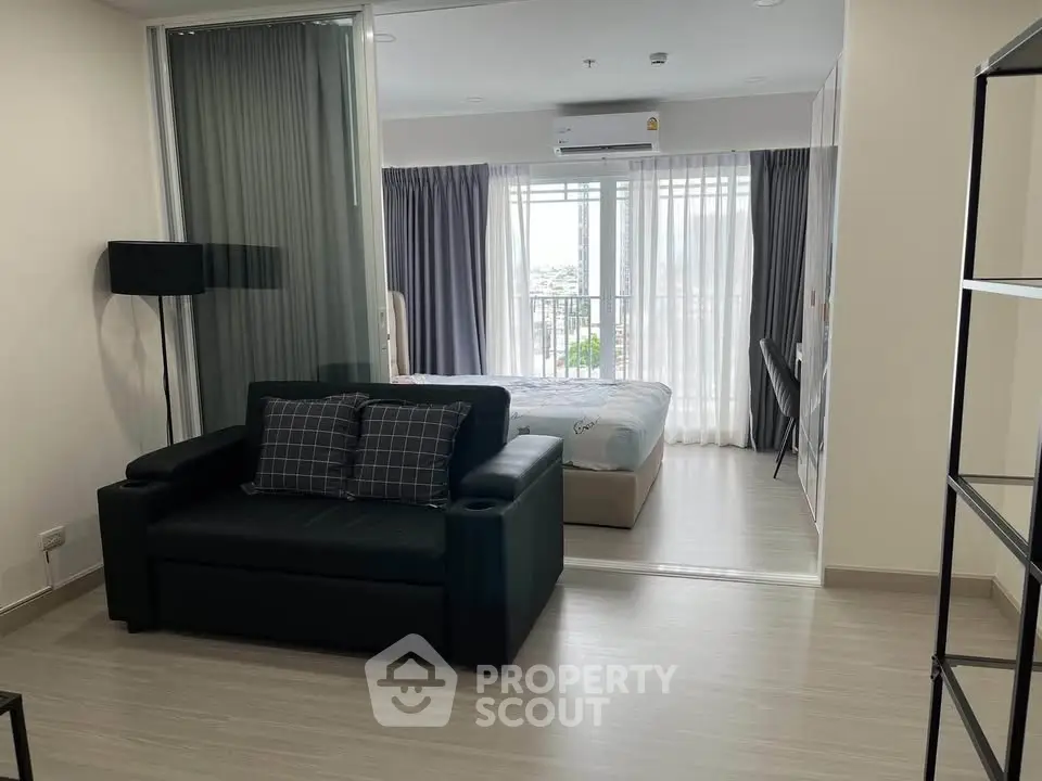 Modern open-plan living room with cozy sofa and bedroom view, featuring floor-to-ceiling windows.