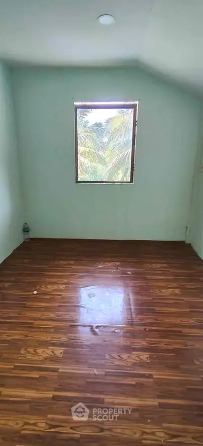 Spacious room with wooden flooring and a window view of lush greenery.