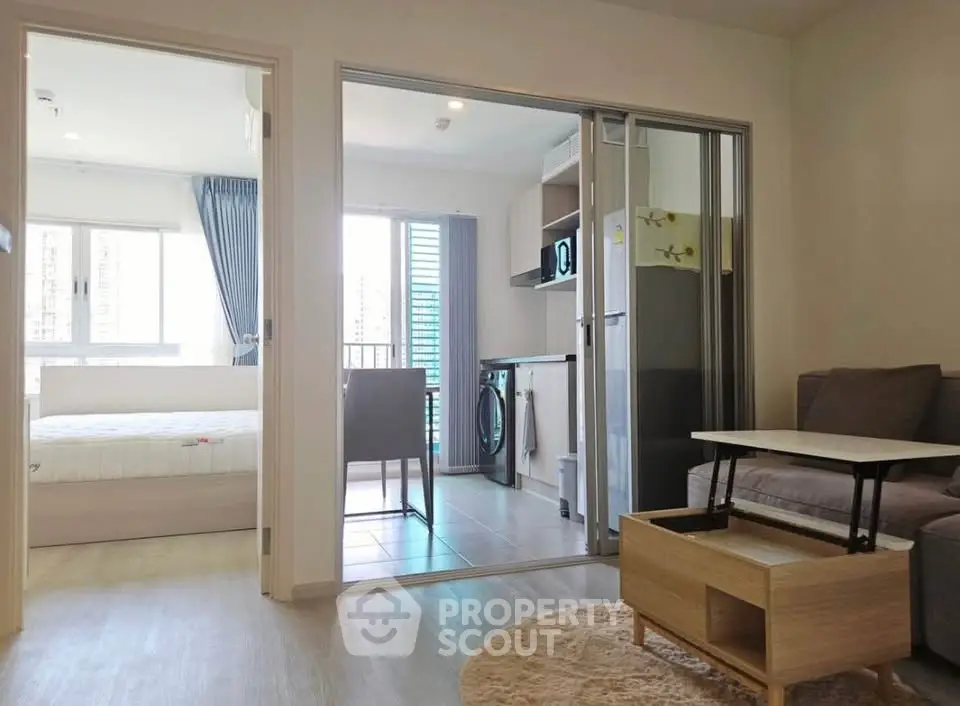 Modern apartment interior with open kitchen and cozy living area, featuring a sliding door to a bright bedroom.