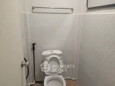 Compact bathroom with white tiles and toilet, featuring a bidet spray for convenience.