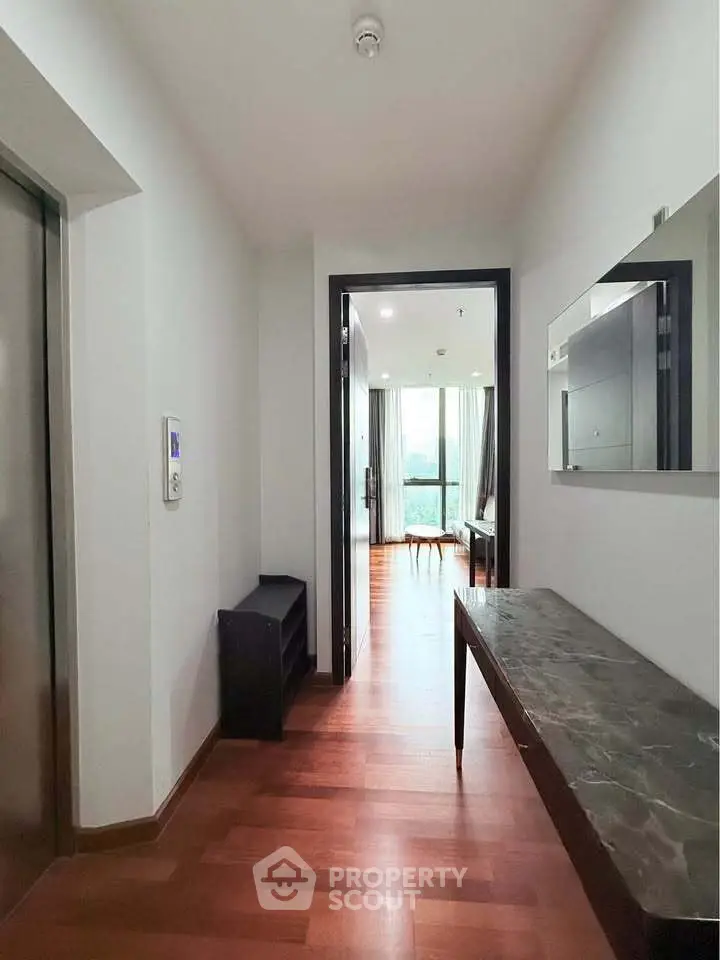 Spacious apartment hallway leading to a bright living room with wooden flooring and modern decor.