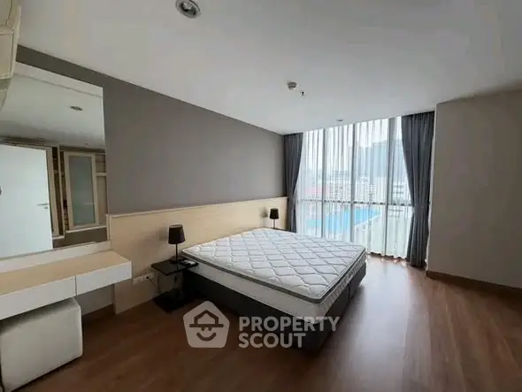 Spacious bedroom with large window and modern furnishings in a stylish apartment.