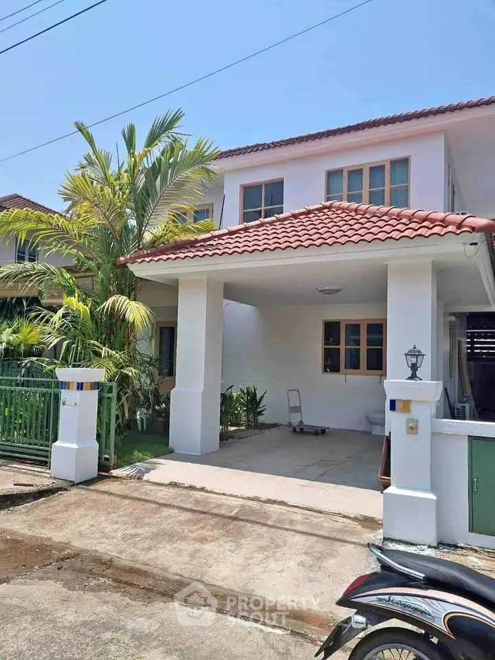 Charming two-story house with red-tiled roof and spacious carport in a serene neighborhood.