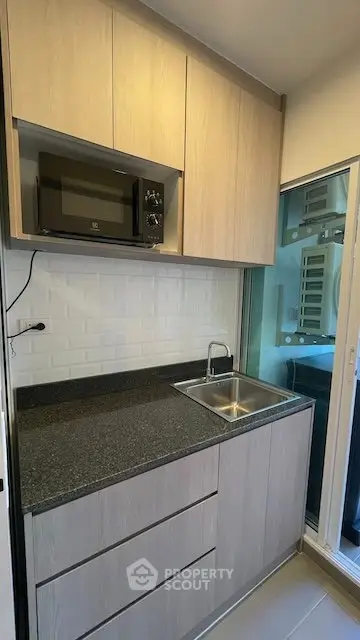 Modern compact kitchen with sleek cabinetry and built-in microwave, featuring a stylish black countertop and stainless steel sink.