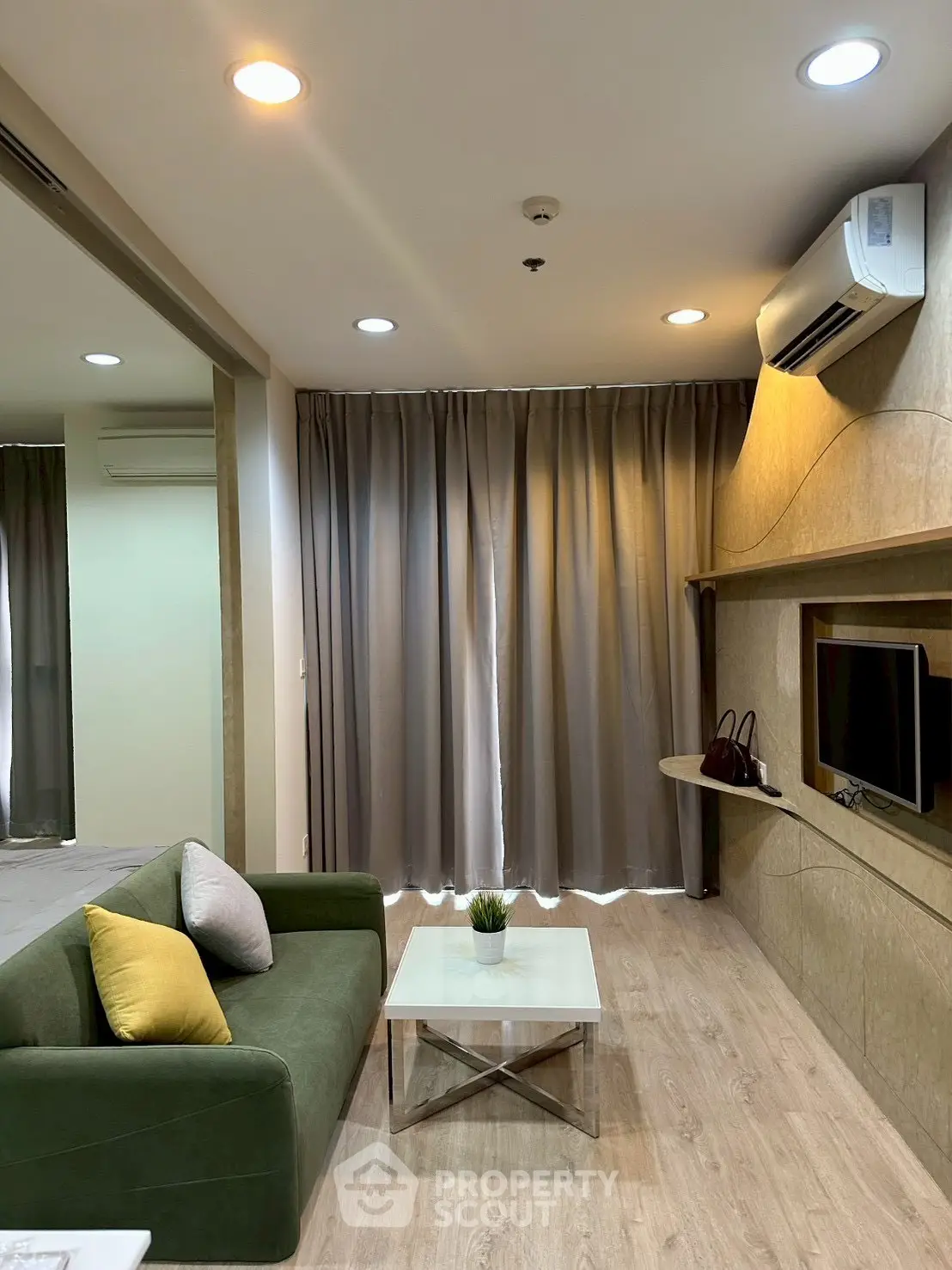Modern living room with green sofa, wall-mounted TV, and air conditioning