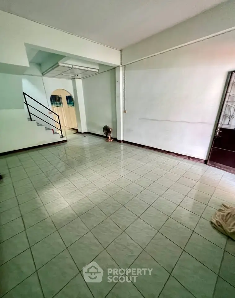 Spacious tiled living room with staircase and natural light, ideal for family gatherings.