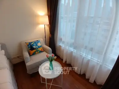 Cozy living room with armchair, lamp, and large window with city view.